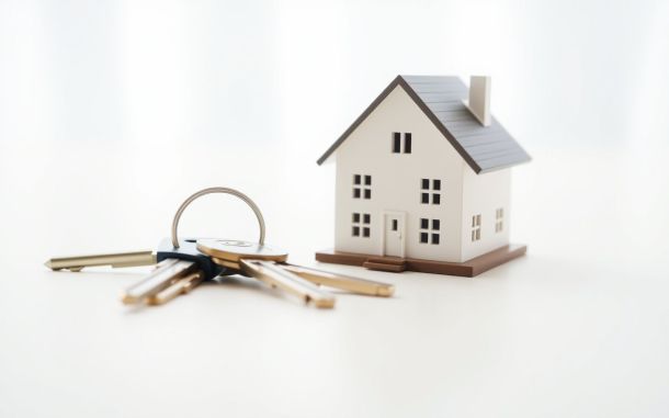 House keys next to a miniature home model symbolizing the pros and cons of turnkey real estate investing.