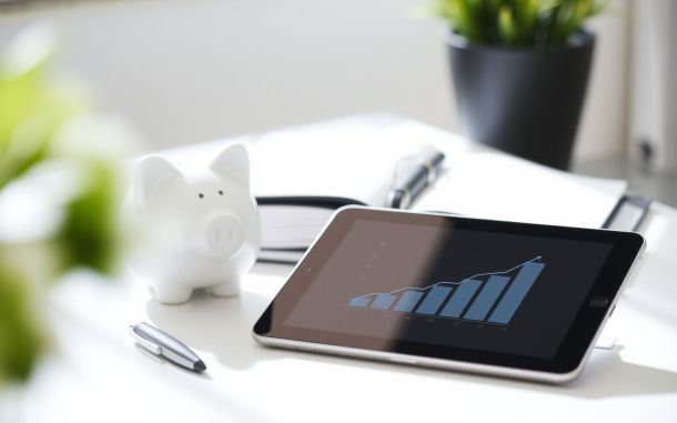Upward graph on tablet and piggy bank on bright desk symbolizing negotiating salary increase during performance review.